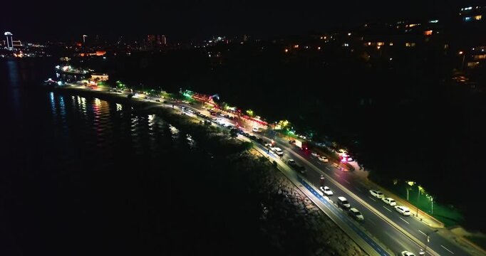 Coastal highway traffic flowing along waterfront at night with colorful city lights reflecting on sea, Uskudar, Istanbul