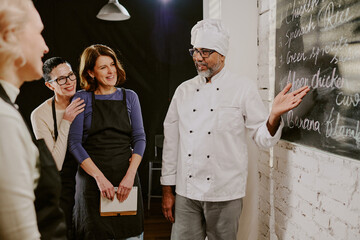 Middle aged man chef explaining cooking techniques to group of Caucasian women in cooking class,...