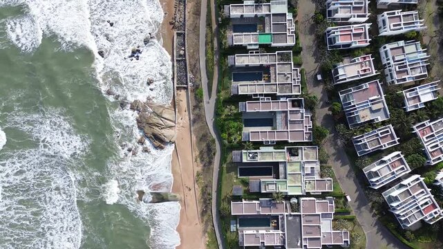 Aerial boom out revealing coastline with half ocean waves and half resort buildings, top view split composition of beach and urban coastal development
