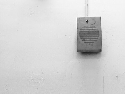 Vintage vintage intercom speaker mounted on a textured white concrete wall.