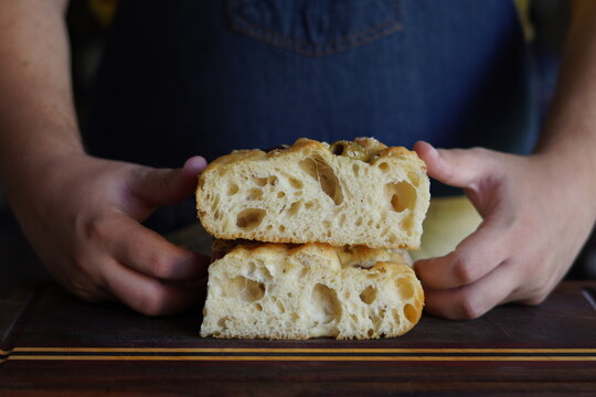 Close up of a fluffy focaccia bread with a crispy, golden crust and hands in the background