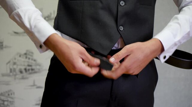 Groom Man Adjusting Black leather Belt with Elegant White Shirt and Tailored Trousers.