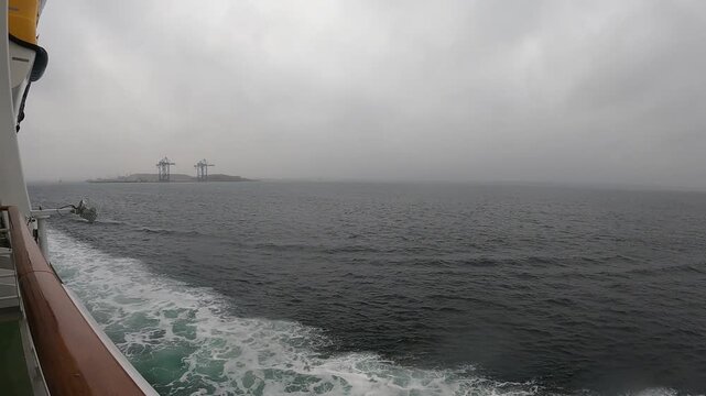 Einfahrt in den Hafen von Kopenhagen bei Regen als Zeitraffer. Blick vom Kreuzfahrtschiff auf modernes Hafenviertel. Reisemotiv mit Copyspace f&uuml;r Tourismus und Seefahrt.