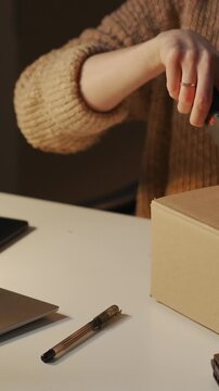 Person carefully unboxing and inspecting bottled liquid product at a tidy workspace, using cutter and packing tools to open and prepare cardboard shipping package