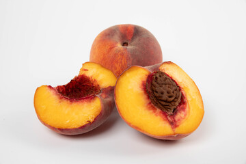 two peaches, one whole and one broken into 2 halves, one half whole and one half pitted, on a white background