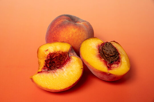 two peaches, one whole and one broken into 2 halves, one half whole and one half pitted, on a orange background