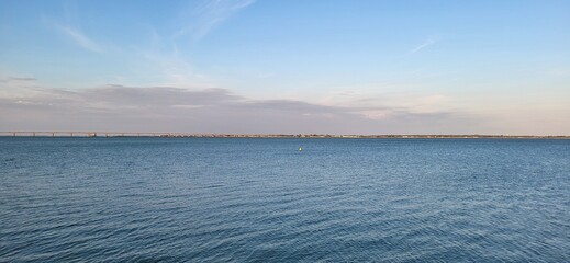 A bridge stretches across a calm body of water, linking two shores bathed in gentle light. A solitary buoy floats at the center, acting as a quiet marker where architecture meets the serenity  © catf