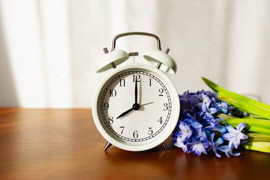 White alarm clock showing 8 am near hyacinth flowers