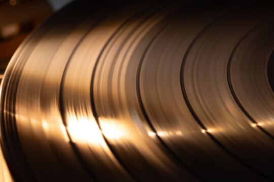 Close-up view of vintage vinyl records displaying grooves and reflections, illuminated by soft lighting, showcasing the texture and detail of the records