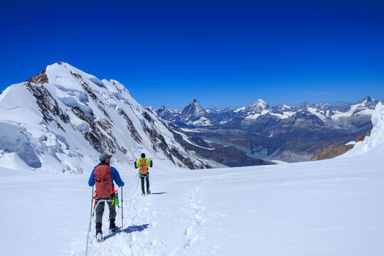 Mountaineers in rope team with crampons descending on glacier Grenzgletscher and mountain panorama with summits Lyskamm, Matterhorn and Dent Blance (left to right) in Pennine Alps, Switzerland