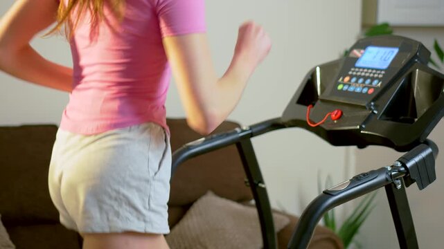 Cardio training of unrecognizable woman running on treadmill with digital display in apartment interior. Smooth jogging pace during daily home workout and endurance exercise session. Healthy lifestyle