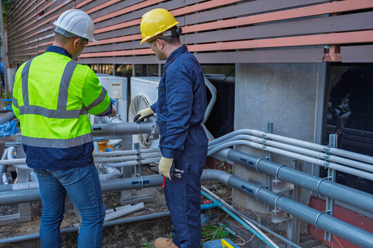 Two professional engineers inspecting industrial air conditioning system outside. Construction workers checking hvac maintenance with clipboard and toolbox at manufacturing factory site plant.