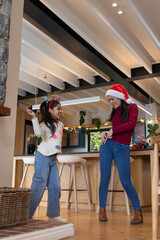 Asian mother and child dancing in kitchen by wooden island wearing Santa hat and reindeer headband