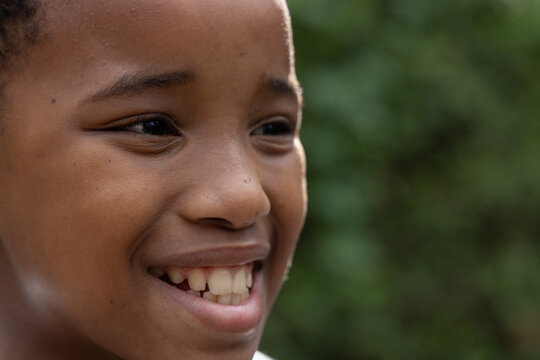 African American child boy smiling, facing right in garden, showing teeth, short hair, light collar