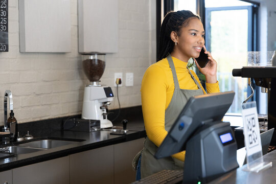 African American woman wearing apron holding phone, using POS at counter with QR sign, copy space