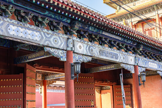 Detailed view of a Chinese gate of Imperial Ancestral Temple with blue and gold dougong brackets, red columns, and studded wooden doors. Imperial craftsmanship in Beijing.