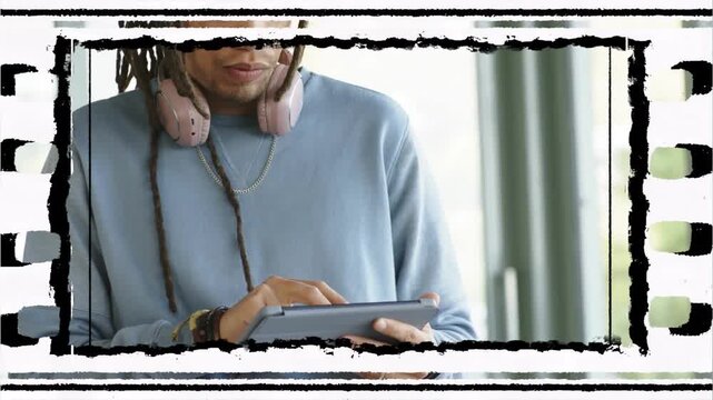 Man tapping tablet, revealing torso and pink headphones, filmstrip framing, reviewing tech