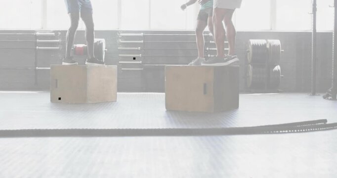 Three men starting set on wooden plyo boxes near backlit windows, stepping, jumping for fitness