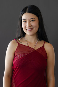 Female posing and smiling in studio, wearing burgundy strappy top with beaded necklace