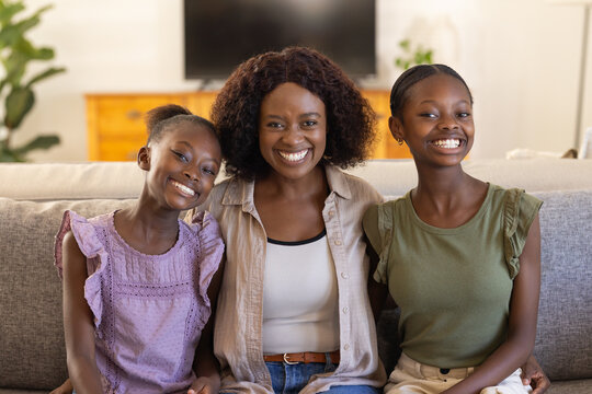 African American female family sitting on gray sofa in living room, mother, teen, child smiling