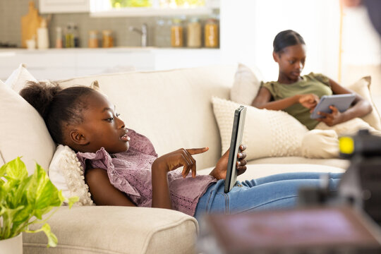 Vertical video: Tapping child in top, jeans, lounging on sofa in living room using tablet for fun