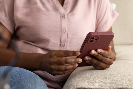 Vertical video: Holding maroon phone, woman scrolling while sitting on beige sofa in pink and denim