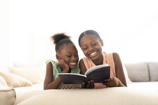 Paperback book is resting open on light sofa with backlit window softening beige cushions