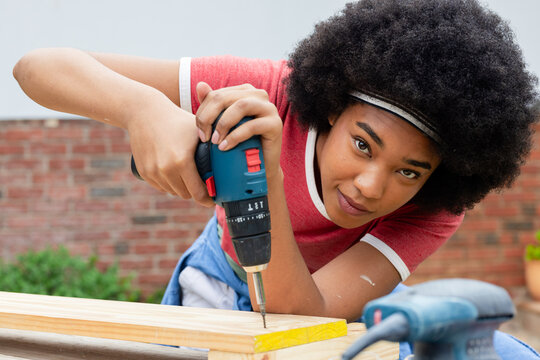 Blue cordless drill is driving screw into yellow-edged plank on backyard workbench, copy space