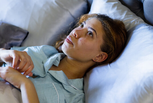 Vertical video: Reclining woman in light blue pajama top propping torso on bed and showing studs