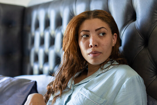 Vertical video: Reacting to soft light, woman sitting by tufted headboard, wearing light blue shirt