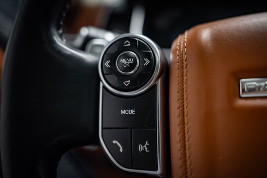 Close up shows left side multifunction controls on a Range Rover wheel, with tan and black stitched leather, MENU OK pad, MODE, phone, and voice buttons in low key light.