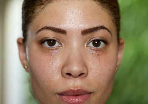 Facing camera, adult woman holding direct gaze in room, with gold stud earrings and eye makeup