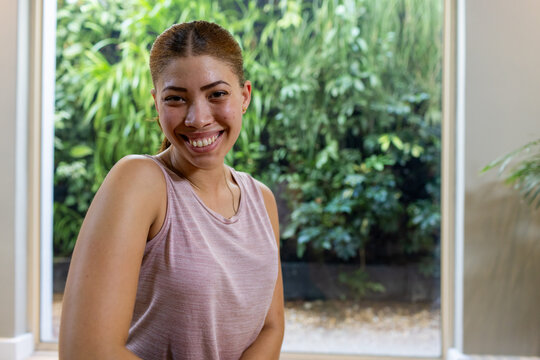 African woman smiling posing at glass door with garden view, wearing pink tank top and necklace