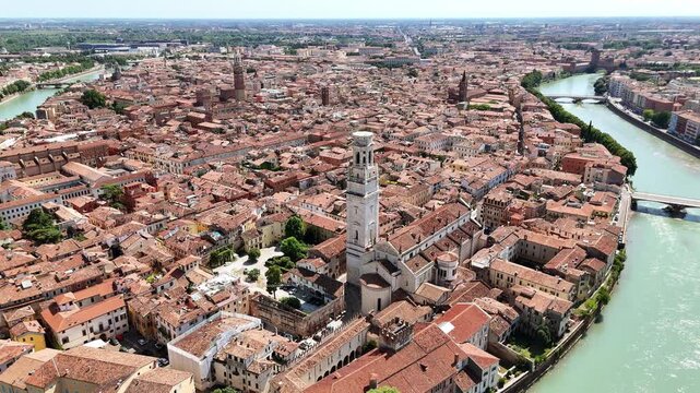 Aerial drone view of Verona's historic city center surrounded by the curved Adige River. The Verona Cathedral bell tower rises above red rooftops and historic architecture
