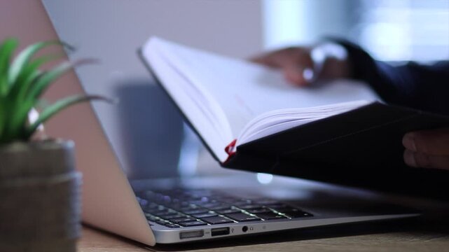 Businessman copying secret data from a notebook and typing a password on a laptop for data security, showcasing cybersecurity and information protection in the office