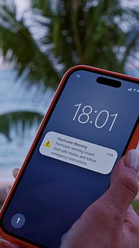 Vertical video. Young Woman Standing on Tropical Beach Holding Smartphone Showing Hurricane Warning Alert Notification While Looking Toward Ocean During Dangerous Storm Situation