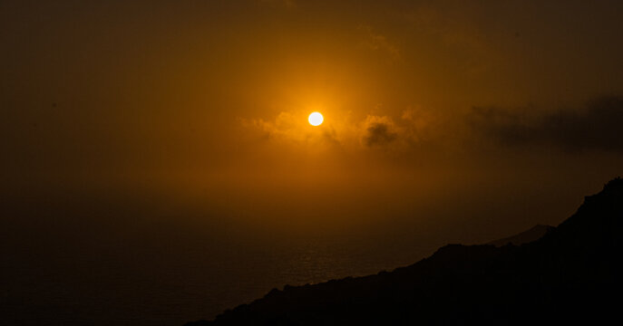 Silueta de costa bajo un sol dorado entre la bruma al atardecer