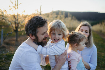 Fototapeta premium Spring portrait of parents with two small children on wlak in blooming orchard.