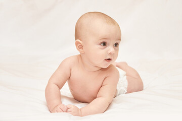 Caucasian Infant Lying On White Blanket Looking Curious And Alert.