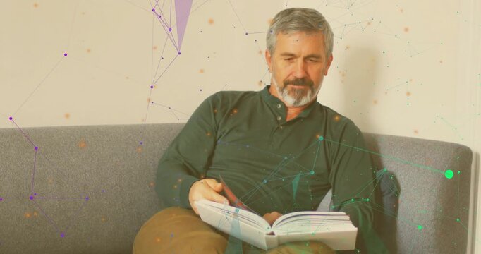 Man on couch turning pages after opening hardback book purple teal network overlaying for education