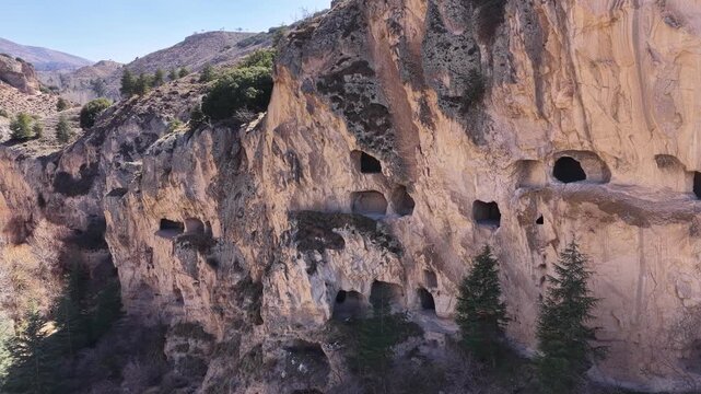 An impressive drone shot of the ancient Teke Sarayı cave settlements, carved into the sheer cliffs of the Seren&ccedil;ay Canyon in Burdur, and the surrounding natural vegetation.