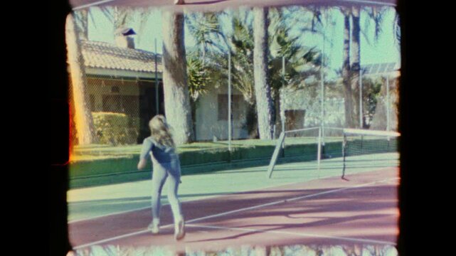 Authentic vintage 8mm home movie footage shows a young blonde girl learning to play tennis on a private court. The nostalgic clip captures childhood innocence and outdoor fun from the 1970s.