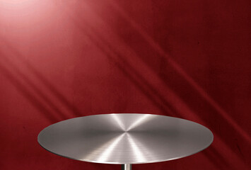 Professional studio product display podium featuring a circular brushed metal stainless steel table top against a textured deep red wall with dramatic light rays and moody diagonal shadows.