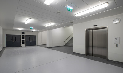 Fototapeta premium Modern hospital corridor interior with elevators and emergency exit signs.