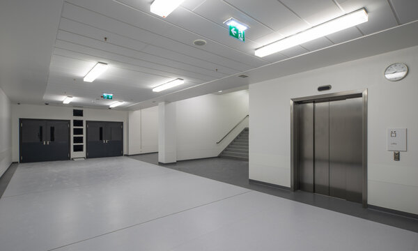 Modern hospital corridor interior with elevators and emergency exit signs.