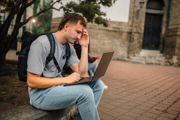Pensive student working on laptop outside university building © Ljustina