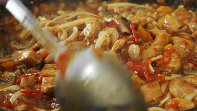 Vegetables with chicken and udon noodles are stewed in a frying pan in Pad Thai sauce and spices. Close-up.
