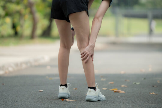 Young woman suffering knee pain after running in park. woman suffering leg cramp after running in park, bending forward and holding painful calf muscle, sports injury and dehydration fitness concept.