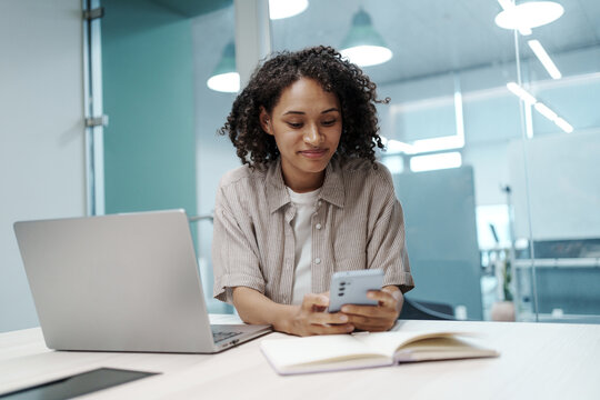 Female Professional At Her Desk Creating Social Media Update While Balancing Gadgets And Notes