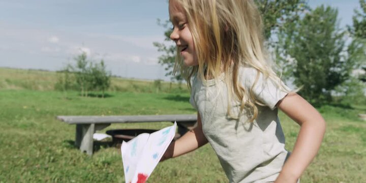 Two children standing in a sunny field with trees and a bench